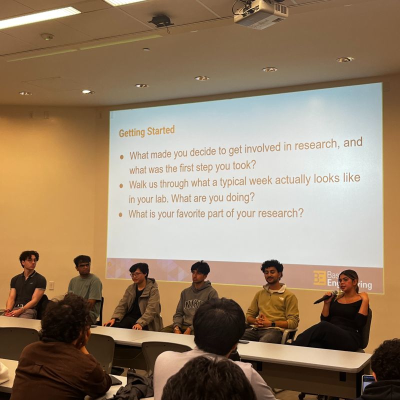 Isabella speaking into a microphone on a student research panel in front of a Baskin Engineering slide